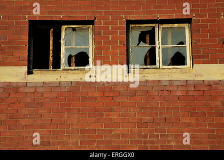 Deux cadres de fenêtre rouille avec du verre brisé dans mur de brique rouge de vieux bâtiment abandonné abandonné Banque D'Images