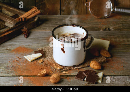 Mug vintage avec du chocolat chaud servi avec des morceaux de chocolat blanc et noir et d'amandes sur la vieille table en bois Banque D'Images