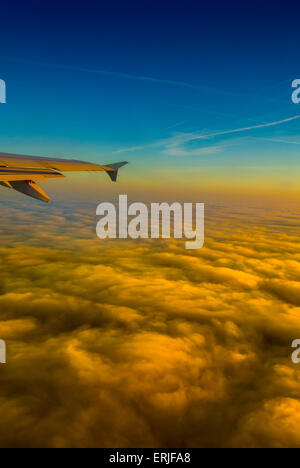 Vue depuis la fenêtre de l'avion au lever du soleil avec ciel bleu et nuages orange doré Banque D'Images