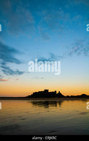 Château de Bamburgh silhouetté contre l'incandescence du coucher et se reflètent dans le sable humide de la plage à marée basse. Lunteren Banque D'Images