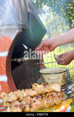 La main de l'appétissant de grillage barbecue de porc sur le feu Banque D'Images