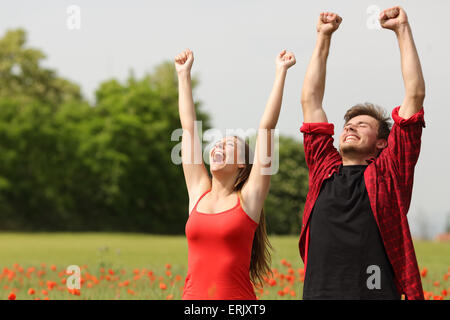 Couple heureux euphorique raising arms dans un champ pays avec les fleurs rouges Banque D'Images