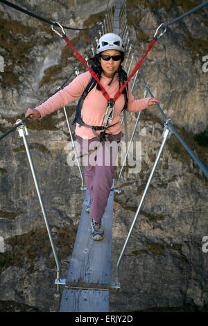 Une jeune femme marche sur un pont tout en s'engageant dans le sport de la Via Ferrata de Val d'isère, Savoie, France. Banque D'Images