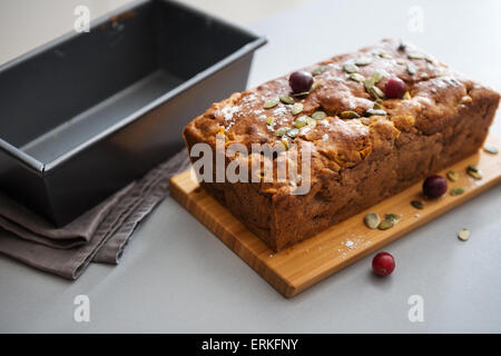 Sur un comptoir de cuisine, une canneberge et cuites au four à pain de graines de citrouille est debout et de refroidissement sur une planche à découper en bois. Banque D'Images