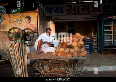 Homme en blanc détendue dhoti de vendre le lait de coco et le jus de canne à sucre à partir de la simple en panier, Rajkot, Gujarat, Inde Banque D'Images