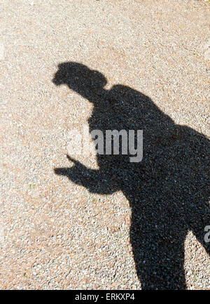 Ombre d'un homme portant un chapeau à large dans la lumière du soleil fait semblant de braquer un fusil avec ses doigts. UK Banque D'Images