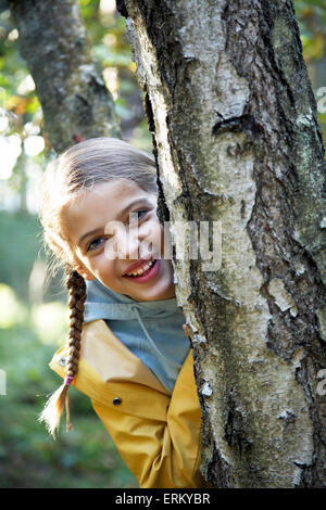 Portrait d'une jeune fille debout derrière un arbre dans une forêt près de Hambourg, Allemagne. Banque D'Images