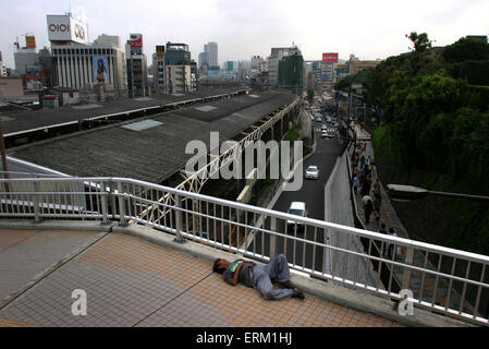 Un sans-abri dort sur un trottoir avec la toile de fond de bâtiments de Tokyo, au Japon. Banque D'Images