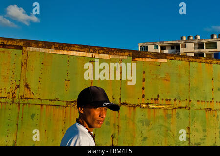 Un jeune homme cubain, portant un chapeau de base-ball, promenades en face d'un contenant dans Alamar, La Havane, Cuba. Banque D'Images