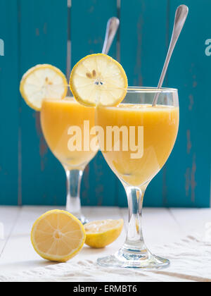 Deux verres de vin jaune frais smoothie aux fruits tropicaux à la mangue et ananas placé sur un tableau blanc. Fond bleu turquoise Banque D'Images