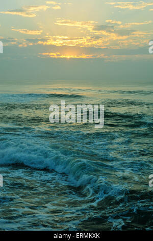 Belle lumière dorée de l'aube reflétant sur les nuages sur l'océan où les vagues se briser sur la côte du KwaZulu-Natal Banque D'Images