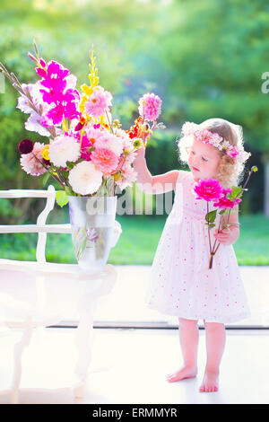 Belle petite fille aux cheveux bouclés vêtue d'une robe blanche fleurs odorantes, bouquet coloré dans un grand vase Banque D'Images