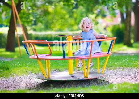 Rire heureux, magnifique petit enfant bébé fille portant une robe bleue s'amuser sur une aire de profiter d'un swing ride Banque D'Images