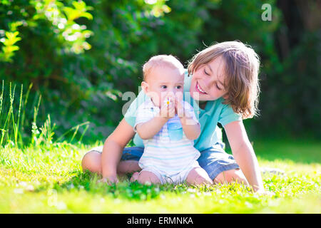 Deux frères, heureux petit garçon de l'école et un petit bébé, jouer ensemble assis sur la pelouse qui sent les fleurs Daisy Banque D'Images