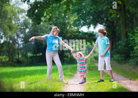 Happy active woman enjoying randonnées avec deux enfants, l'âge scolaire et mignon garçon curly bébé fille marcher dans la forêt de bois de pin Banque D'Images