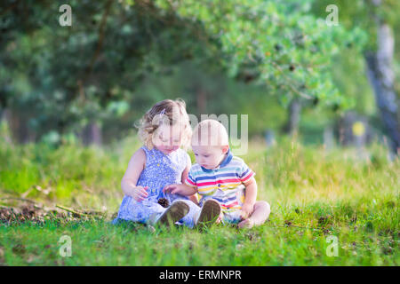 Heureux les petits enfants, adorable bébé fille dans une robe bleue et d'un mignon petit garçon, frère et sœur, jouer avec des pommes de pin Banque D'Images