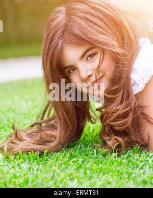 Cute little girl couchée sur l'herbe verte fraîche, avoir du plaisir sur le terrain en plein air, se relaxer sur cour, heureux et insouciant de l'enfance Banque D'Images