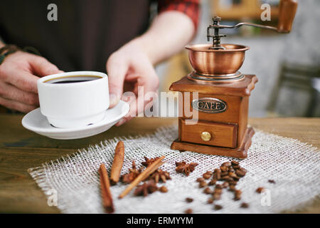 Moulin à café en bois, les grains de café, l'anis étoilé, le bâton de cannelle sur serviette et tasse de café noir dans les mains barista Banque D'Images