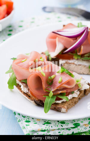 Les sandwiches ouverts avec du jambon, tomates et roquette sur plaque, selective focus Banque D'Images