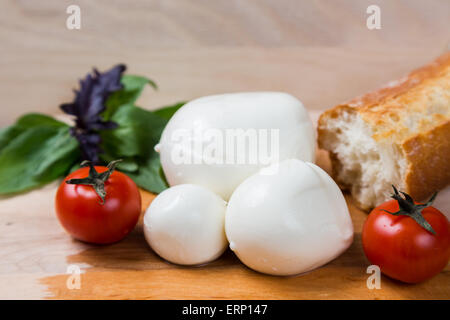 La mozzarella billes taille différentes avec des tomates cerise, le pain et le basilic sur fond de bois Banque D'Images