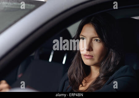 Voir à travers le pare-brise avec reflets de lumières d'une jeune femme sérieuse conduisant sa voiture dans la nuit alors qu'elle travaille accueil Banque D'Images