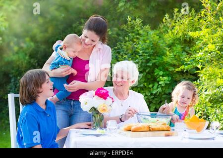 Heureux grand-mère en train de déjeuner avec sa famille - jeune femme et trois enfants, de manger de la viande grillée, salade, pain dans le jardin Banque D'Images