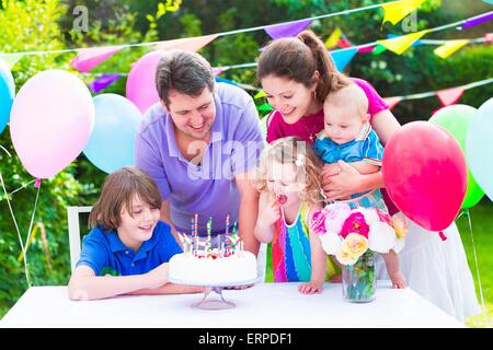 Professionnels grande famille avec trois enfants bénéficiant d'anniversaire avec gâteau blowing candles en jardin décoré avec des ballons et des bannières Banque D'Images