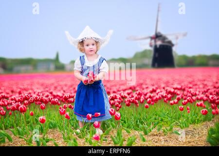 Girl wearing traditionnel néerlandais costume national robe et chapeau jouant dans un champ de tulipes en fleurs à côté d'un moulin Banque D'Images