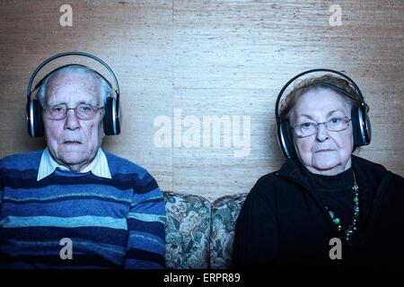 Parution du modèle. Senior couple sitting on sofa portant des écouteurs. Banque D'Images