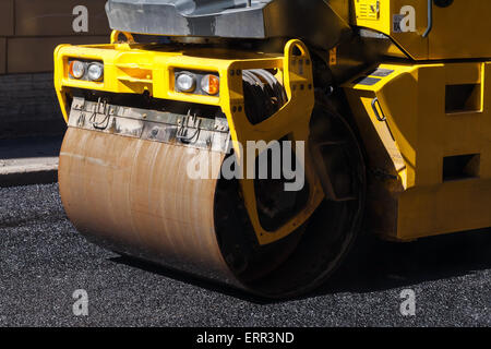 La route en milieu urbain est en cours de construction, de l'asphaltage en cours, fragment de rouleau jaune Banque D'Images