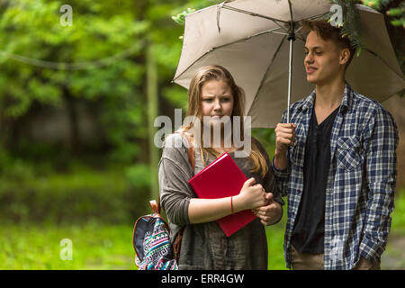 Jeune couple d'étudiants fille avec un livre et le type avec le parapluie à l'extérieur. Banque D'Images