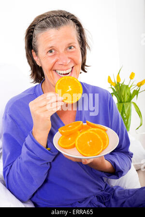 Femme assise au lit et manger des oranges Banque D'Images