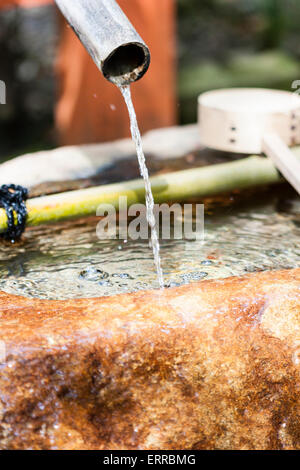 Près, une fontaine de purification, appelée temizuya ou chozuya, dans un sanctuaire Shinto Yasaka à Kyoto. Eau versant d'un tuyau de bambou vert dans le bassin. Banque D'Images