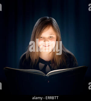 Jeune fille aux cheveux longs de lire un livre avec lumière rougeoyante Banque D'Images