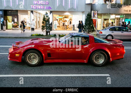 Le ginza la nuit à Tokyo. Une super voiture rouge, une corvette modifiée, en passant dans la rue avec le conducteur tourné pour regarder le spectateur. Banque D'Images