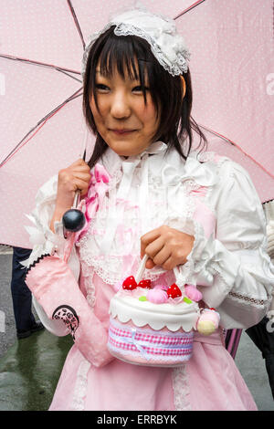 Jeune femme japonaise vêtue de style 'Sweet Lolita' à Harajuku, Tokyo. Porter des vêtements roses et blancs et tenir un parapluie rose et un sac à main pour gâteaux. Banque D'Images