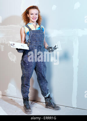 Portrait of a smiling young woman construction travailleur avec une truelle et couteau à mastic réparer drywall Banque D'Images