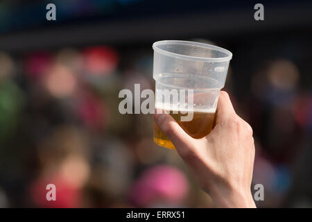Homme hand holding up bière dans un verre en plastique à l'événement en plein air Banque D'Images
