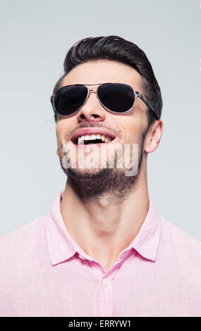 Closeup portrait of a young man laughing in sunglasses sur fond gris Banque D'Images