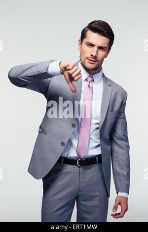 Confident businessman showing thumb down signer sur fond gris. Looking at camera Banque D'Images