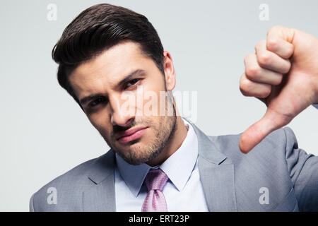 Handsome businessman showing thumb down signer sur fond gris. Looking at camera Banque D'Images