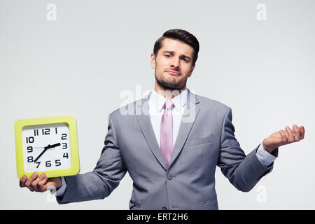 Businessman holding clock et copyspace sur fond gris. Looking at camera Banque D'Images