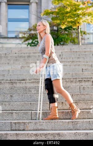 Femme blonde avec des béquilles de marcher dans les escaliers Banque D'Images