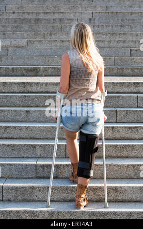 Femme blonde avec des béquilles de marcher dans les escaliers Banque D'Images