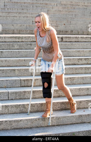 Femme blonde avec des béquilles de marcher dans les escaliers Banque D'Images