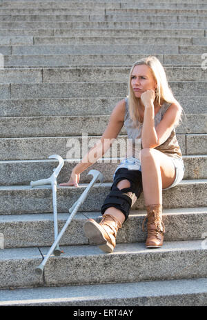 Femme blonde avec des béquilles sitting on stairs Banque D'Images