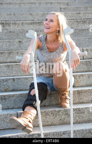 Femme blonde avec des béquilles sitting on stairs Banque D'Images