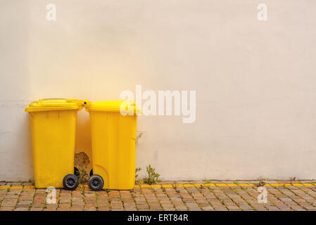 Deux bacs de recyclage en plastique jaune dans la rue contre le mur blanc et vide comme l'espace pour copier du texte, des images aux couleurs Banque D'Images