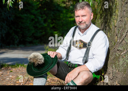 L'homme en costume traditionnel bavarois assis par un arbre Banque D'Images