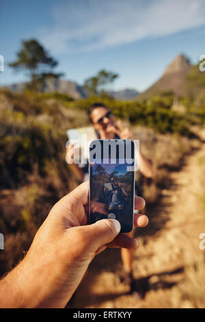 L'homme à prendre des photos sur une jeune femme avec son smartphone. L'accent sur téléphone mobile dans la main. Couple hiking in countryside. Banque D'Images